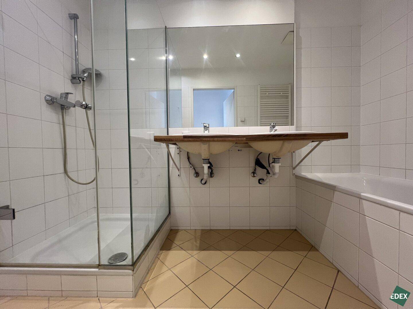 Geräumiges Badezimmer mit Doppelwaschbecken, Dusche und Badewanne, gefliest in hellen Tönen.