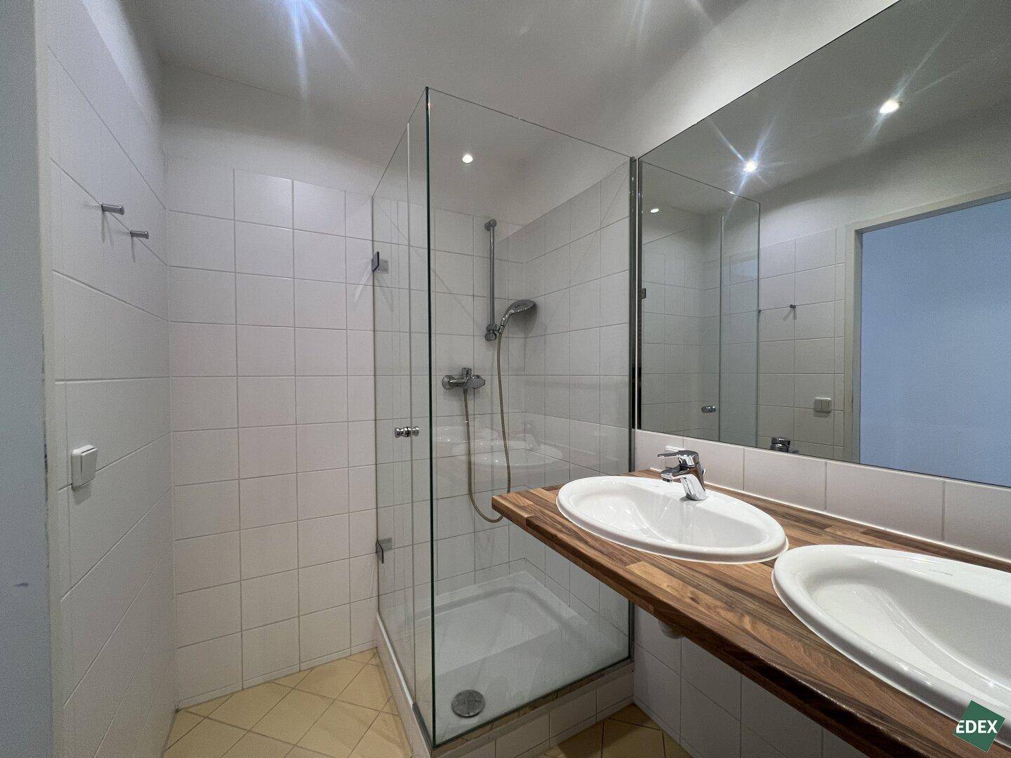 Modernes Badezimmer mit Doppelwaschbecken, großer Spiegelfläche und begehbarer Dusche.