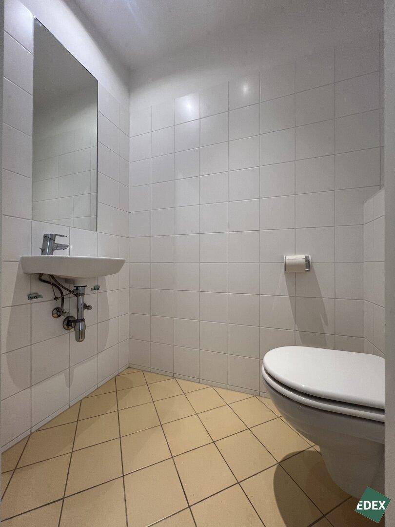 Separates Gäste-WC mit Waschbecken und Toilette, gefliest in hellen Farben und mit Spiegel.