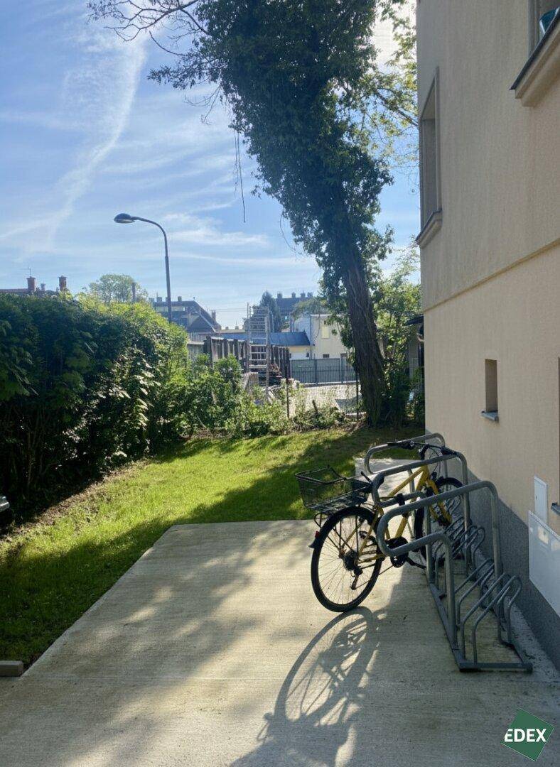 Außenbereich des Gebäudes mit Fahrradständern und Grünfläche unter blauem Himmel, praktisch und hell.