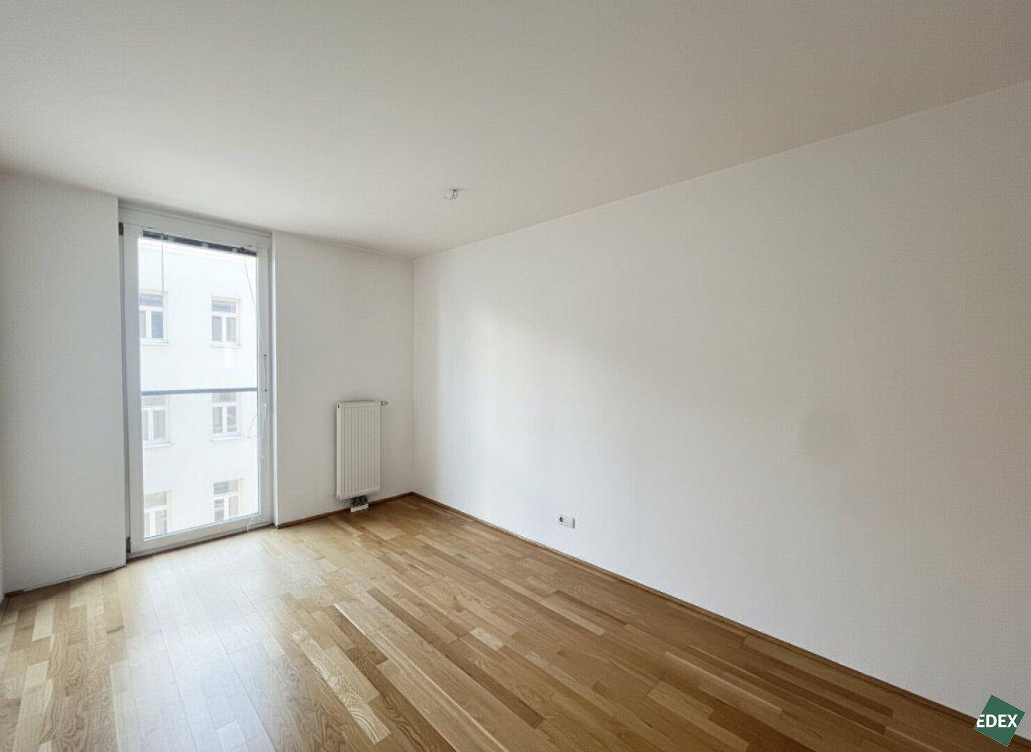 Helles Zimmer mit Parkettboden und großem Fenster, ideal als Schlafzimmer oder Arbeitszimmer.