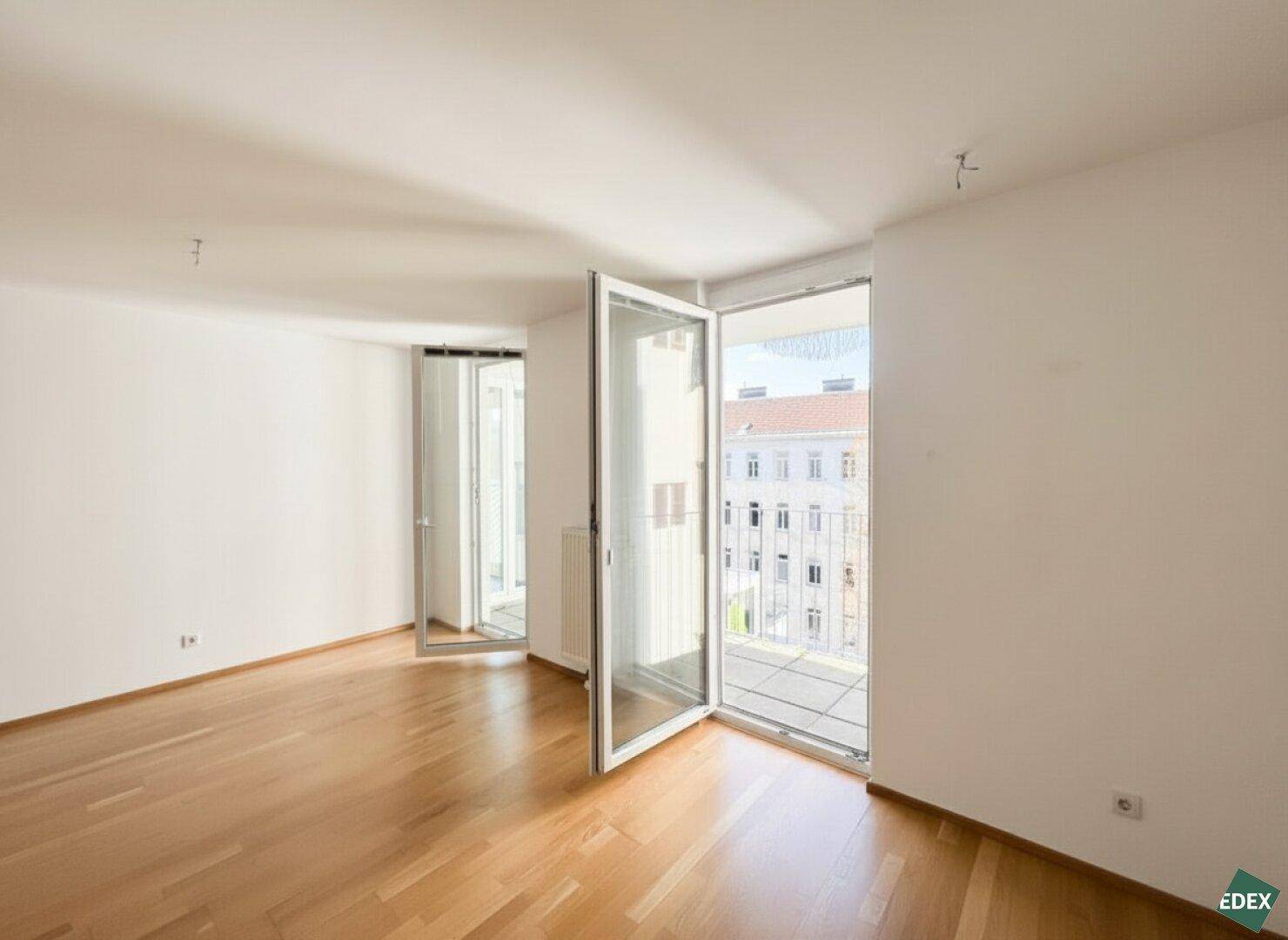 Lichtdurchflutetes Zimmer mit Parkettboden und zwei Balkontüren, die einen Blick nach draußen bieten.