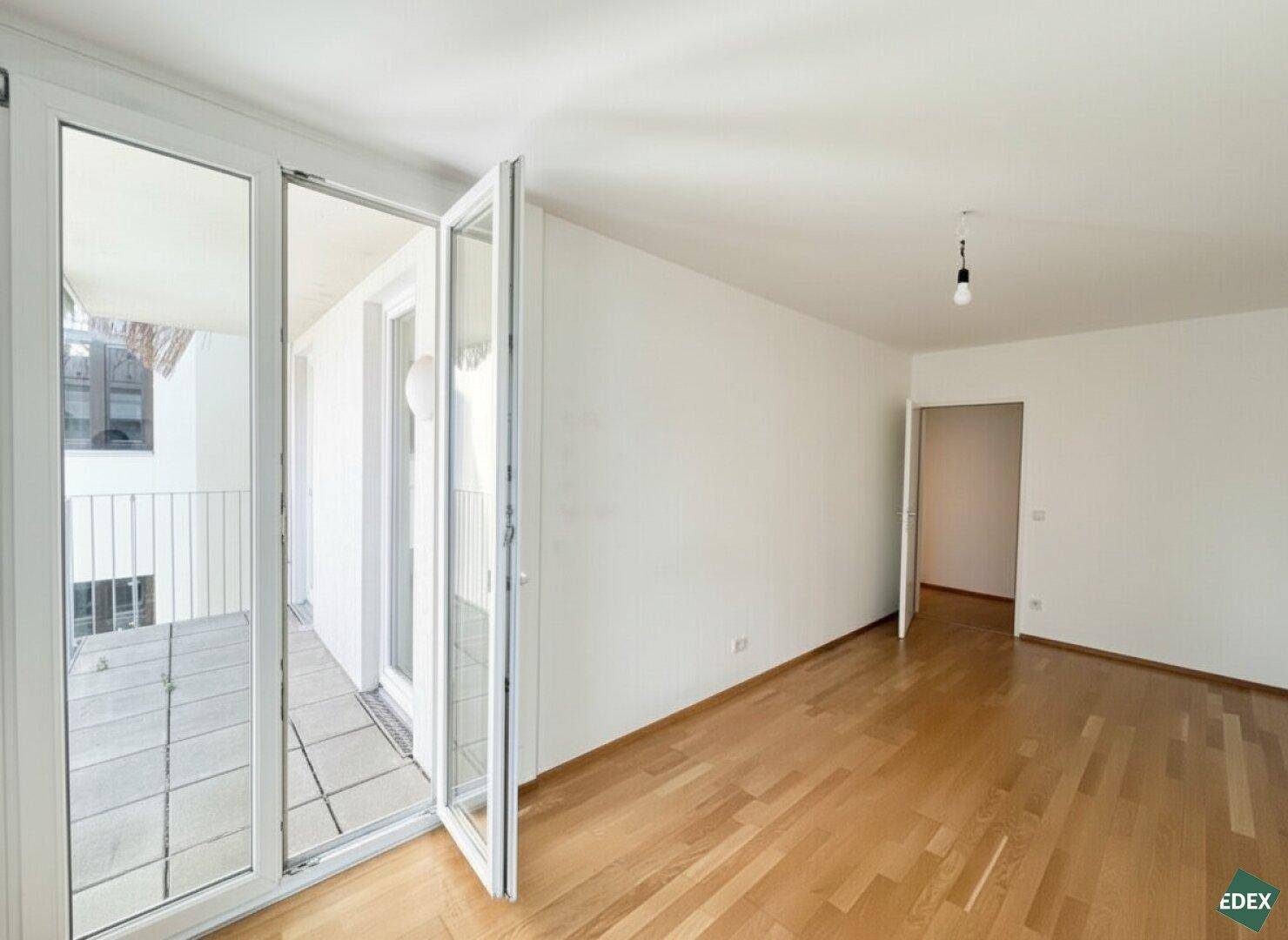 Geräumiges Zimmer mit Parkettboden und Balkonzugang, bietet viel Tageslicht und eine angenehme Atmosphäre.