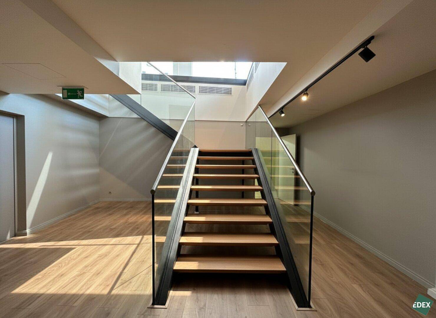 Moderne Treppe mit Holzstufen und Glasgeländer, die zu einem hellen Obergeschoss mit Oberlicht führt.