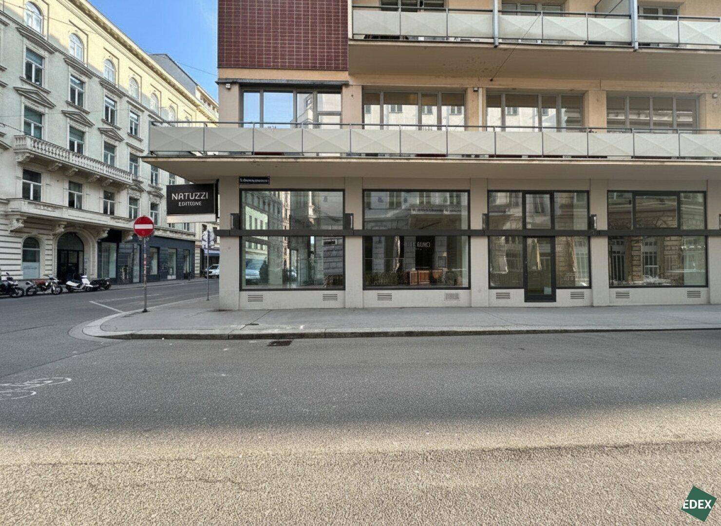 Moderne Geschäftsfassade an einer Straßenecke mit großen Schaufenstern und umliegenden Stadtgebäuden.