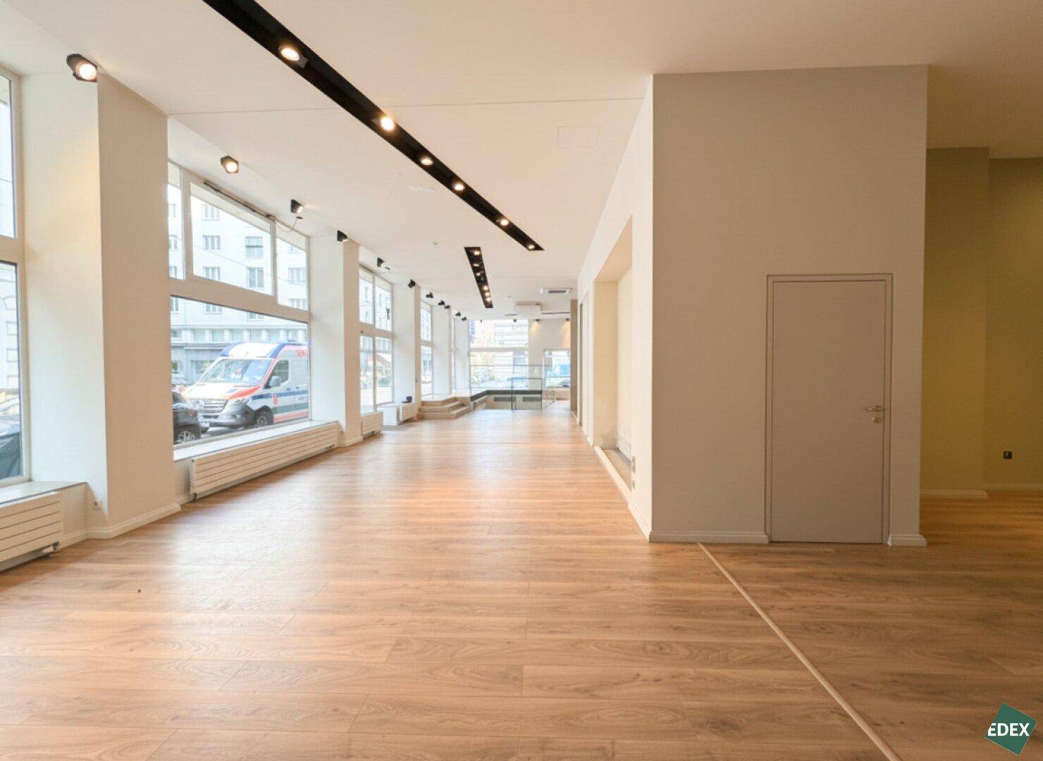 Weitläufiger Geschäftsraum mit durchgehenden Fensterfronten, hellem Holzboden und schlichter, moderner Ästhetik.