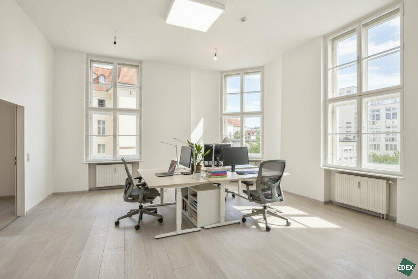 Modern eingerichtetes Büro mit mehreren Arbeitsplätzen, großen Fenstern und viel natürlichem Licht.