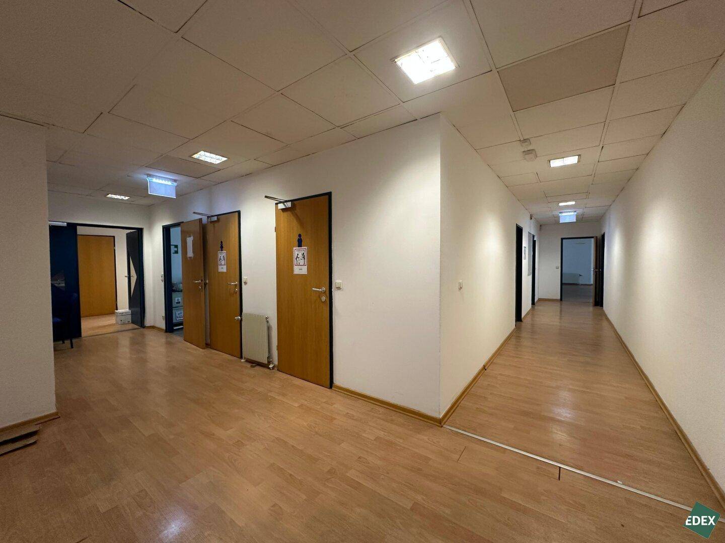 Langer Flur mit mehreren Türen zu Büros oder Sanitäranlagen. Der Boden ist mit hellem Laminat ausgelegt.