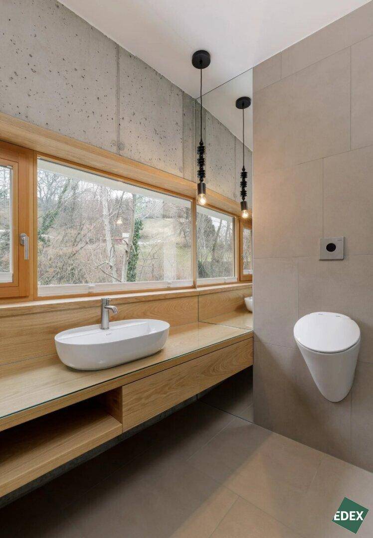 Modernes Badezimmer mit Holzwaschtisch, ovalem Waschbecken und Urinal, mit Blick ins Grüne.