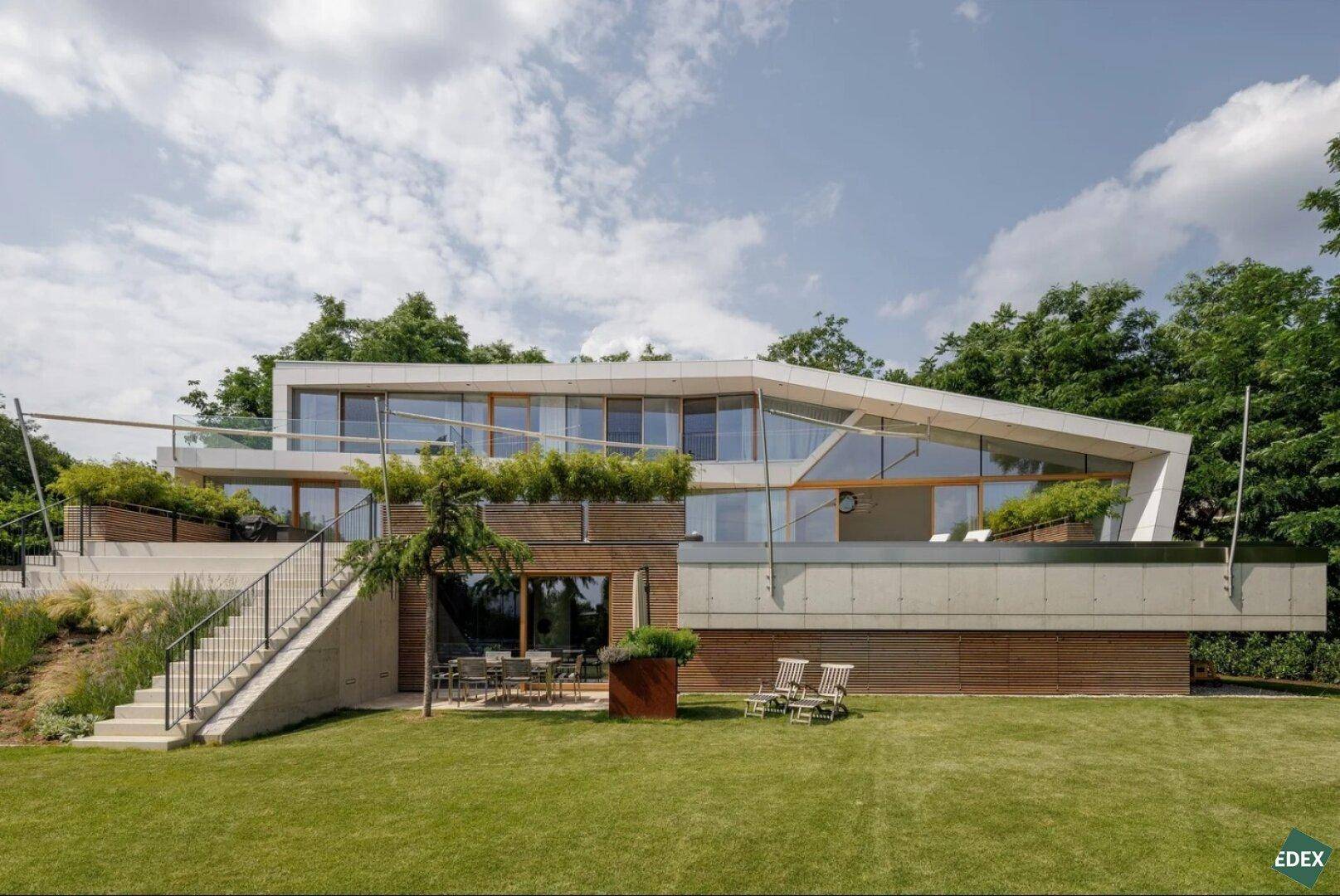 Elegante moderne Villa mit weitläufigem Rasen, Holzverkleidung und großen Fensterfronten.
