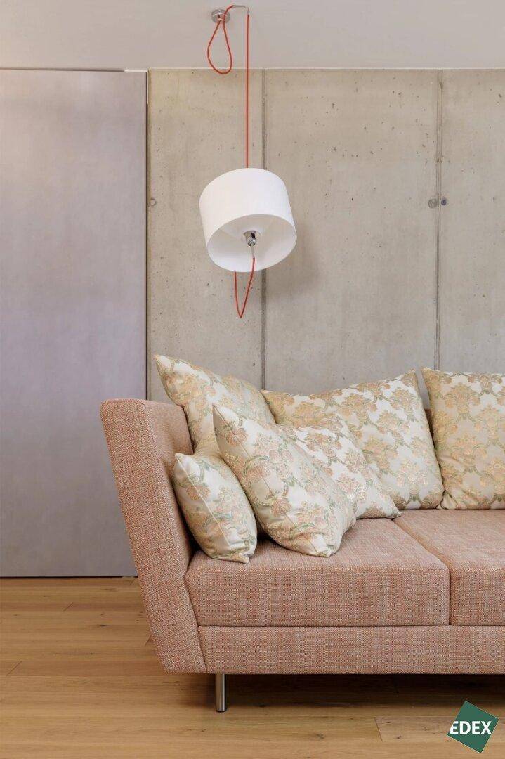 Gemütliches Wohnzimmer mit beigem Sofa, gemusterten Kissen und moderner Pendelleuchte.
