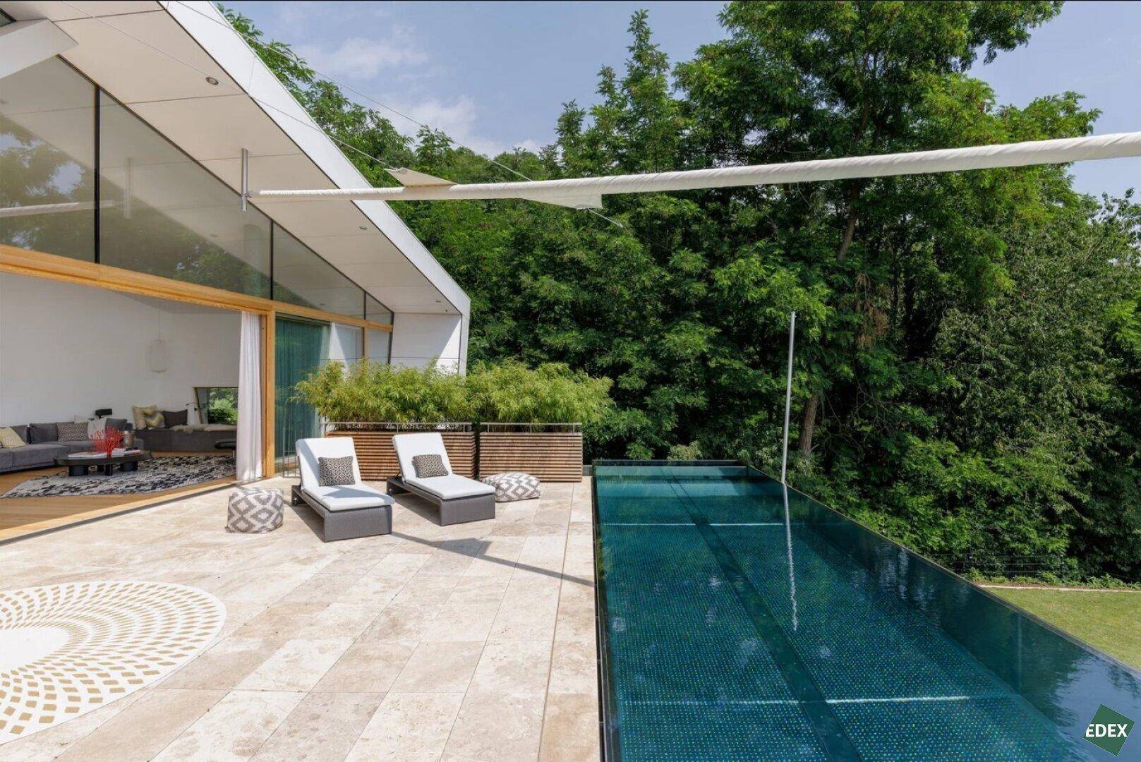 Sonnenterrasse mit Infinity-Pool, Liegestühlen und Blick auf die umliegende Natur.