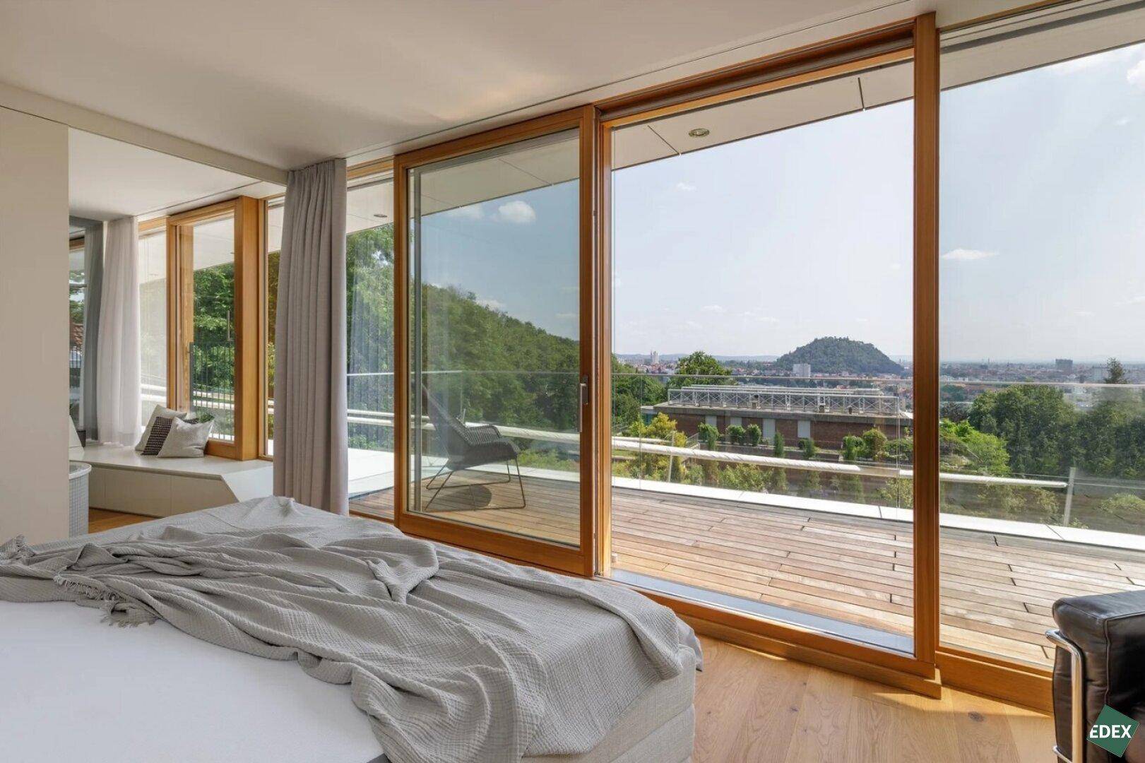 Helles Schlafzimmer mit Holzboden, großen Schiebetüren und Panoramablick über die Stadt und Landschaft.