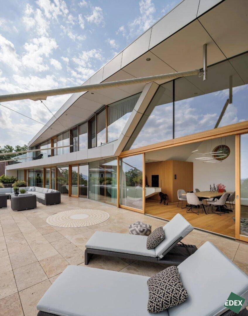 Weitläufige Terrasse mit Liegestühlen und Zugang zum Innenbereich durch große Glasschiebetüren.