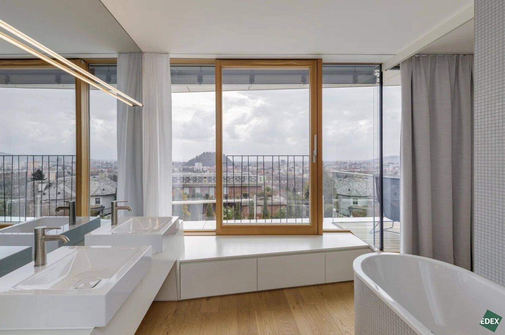 Luxuriöses Badezimmer mit Doppelwaschbecken, Badewanne und weitem Blick durch große Fenster.