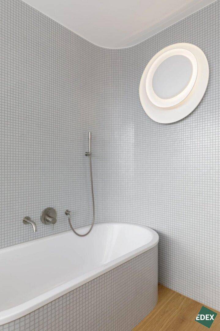 Modernes Badezimmer mit Badewanne und kleinen grauen Mosaikfliesen an den Wänden.