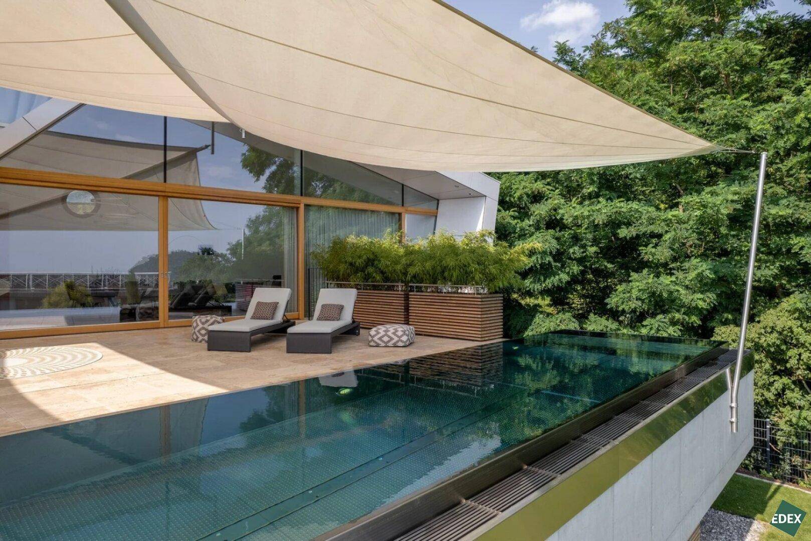 Sonnenterrasse mit Pool, Liegestühlen und großem Sonnensegel für angenehmen Schatten.