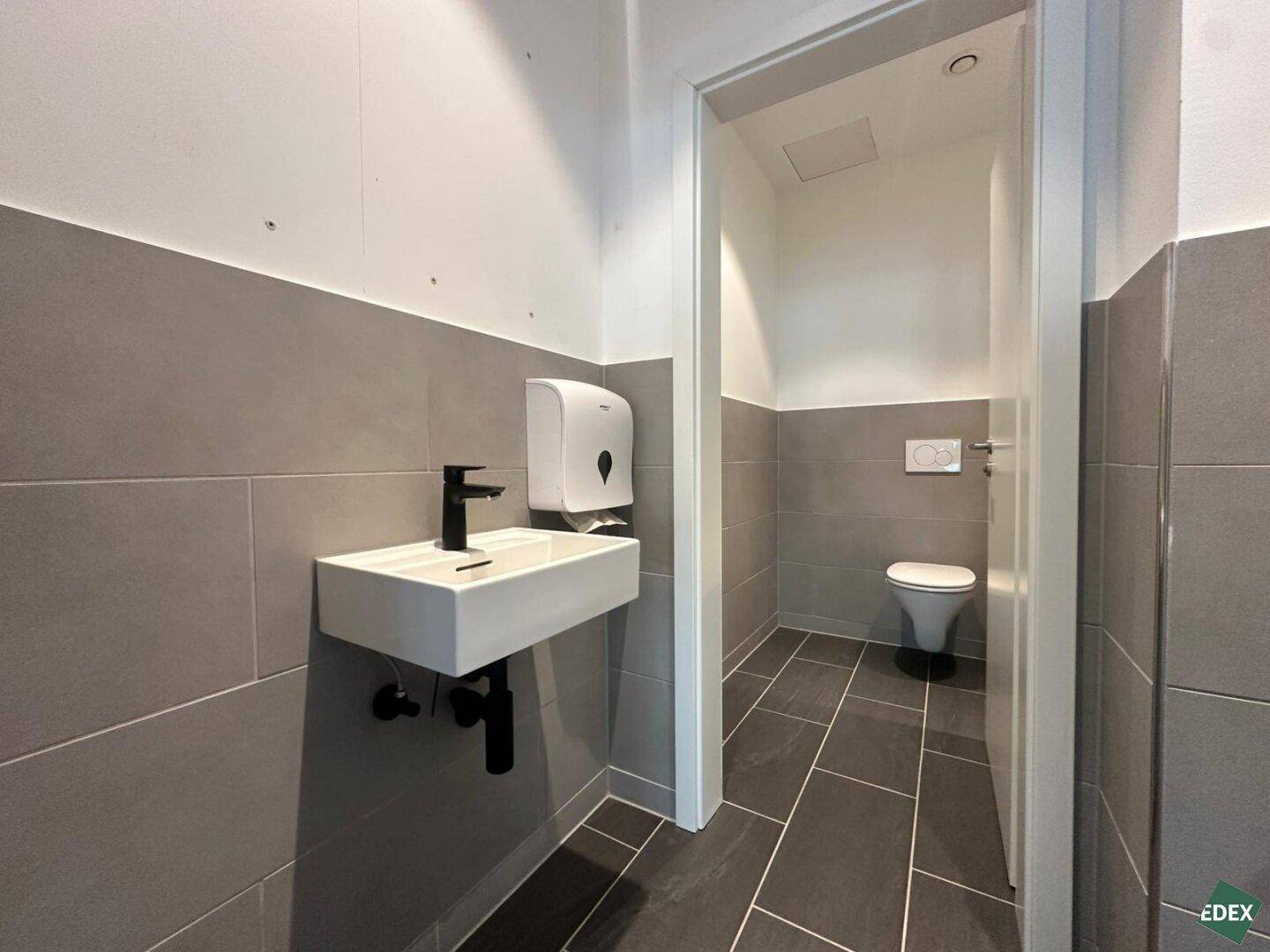Moderne Toilette mit Waschbecken, dunklen Fliesen und weißer Wandgestaltung in neuwertigem Zustand.