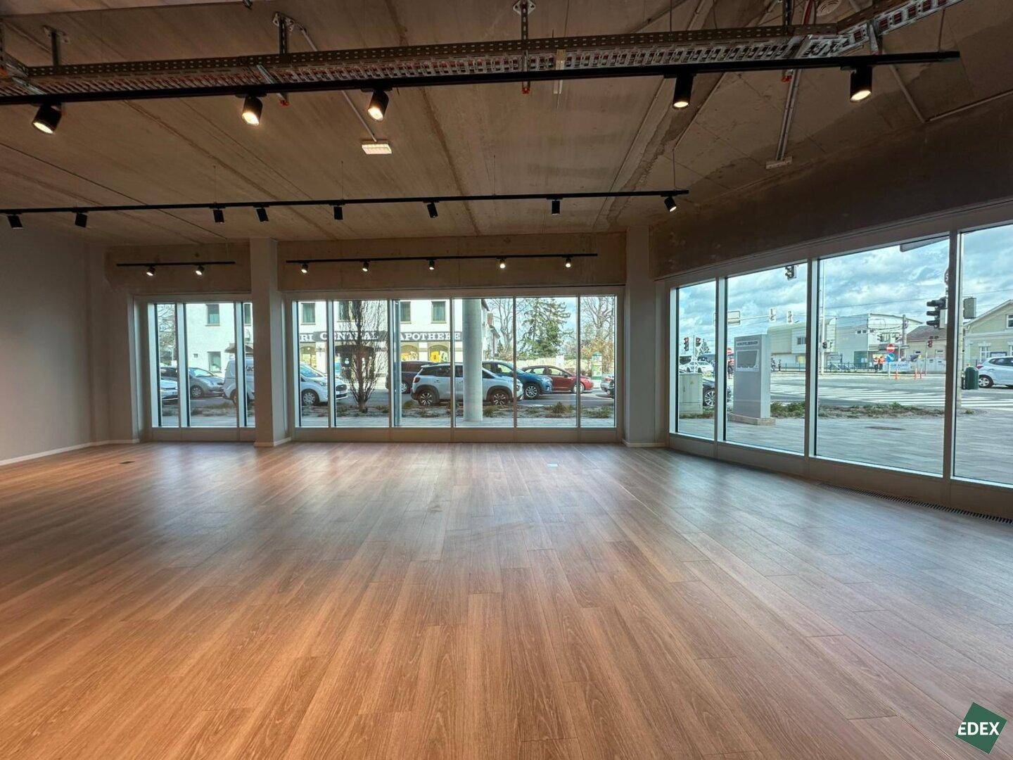 Weitläufiger Gewerberaum mit großen Schaufenstern zur Straße und hellem Laminatboden in modernem Design.