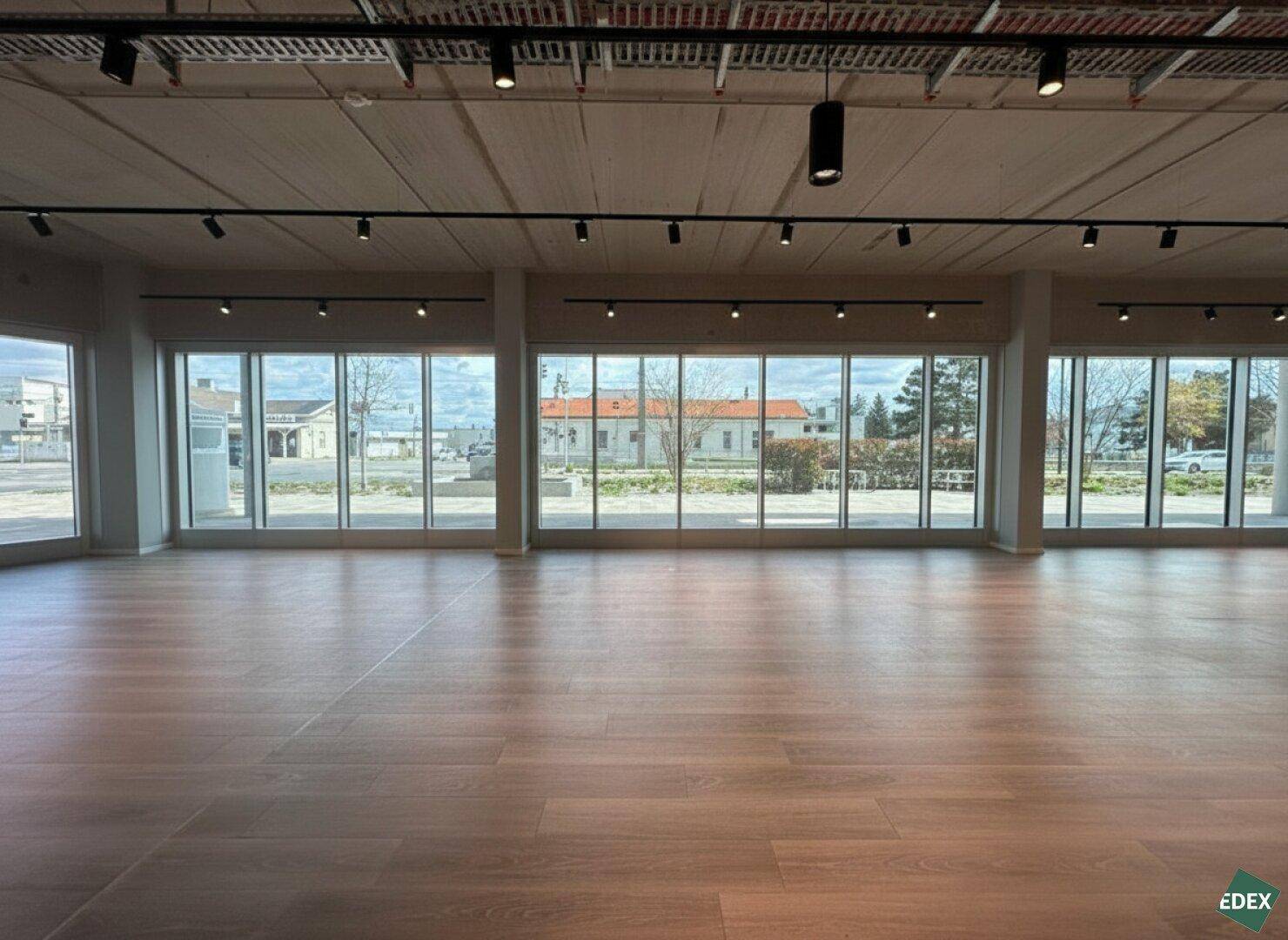 Heller Gewerberaum mit breiter Fensterfront, Blick auf die Umgebung und modernem Bodenbelag in neuwertigem Zustand.