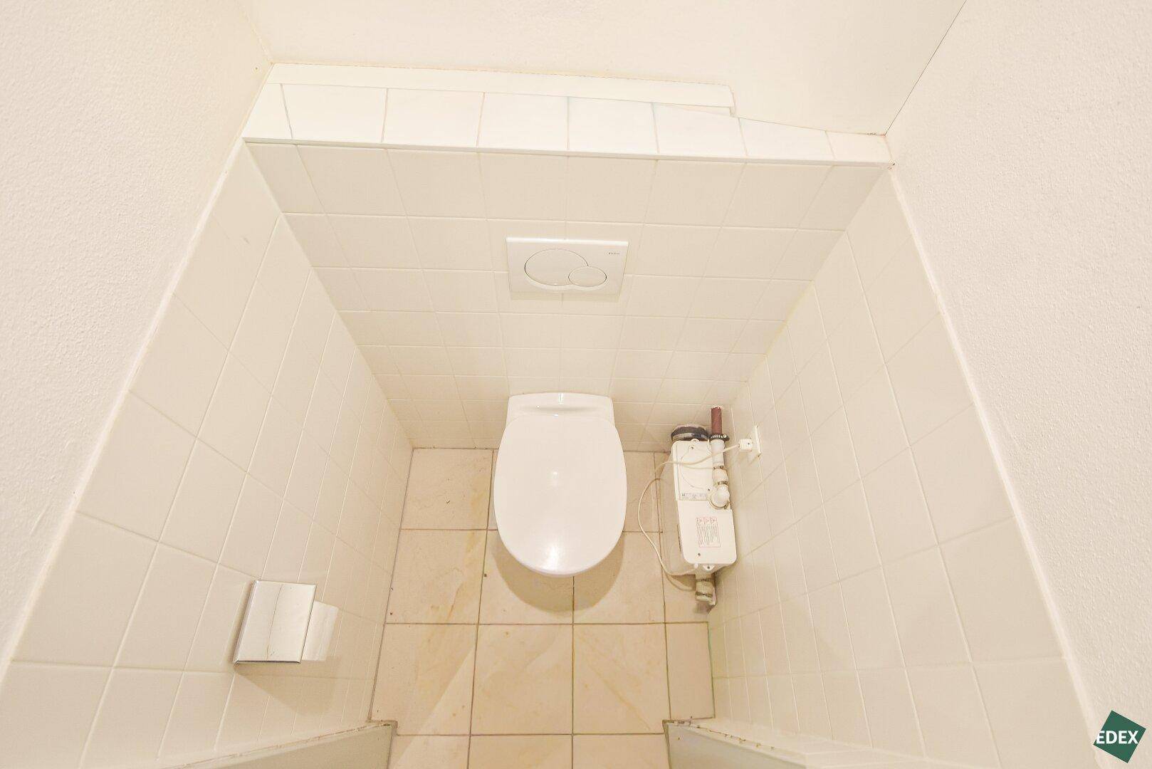 Saubere Toilette mit Wand-WC und gefliesten Wänden in einem funktionalen, hellen Raum.