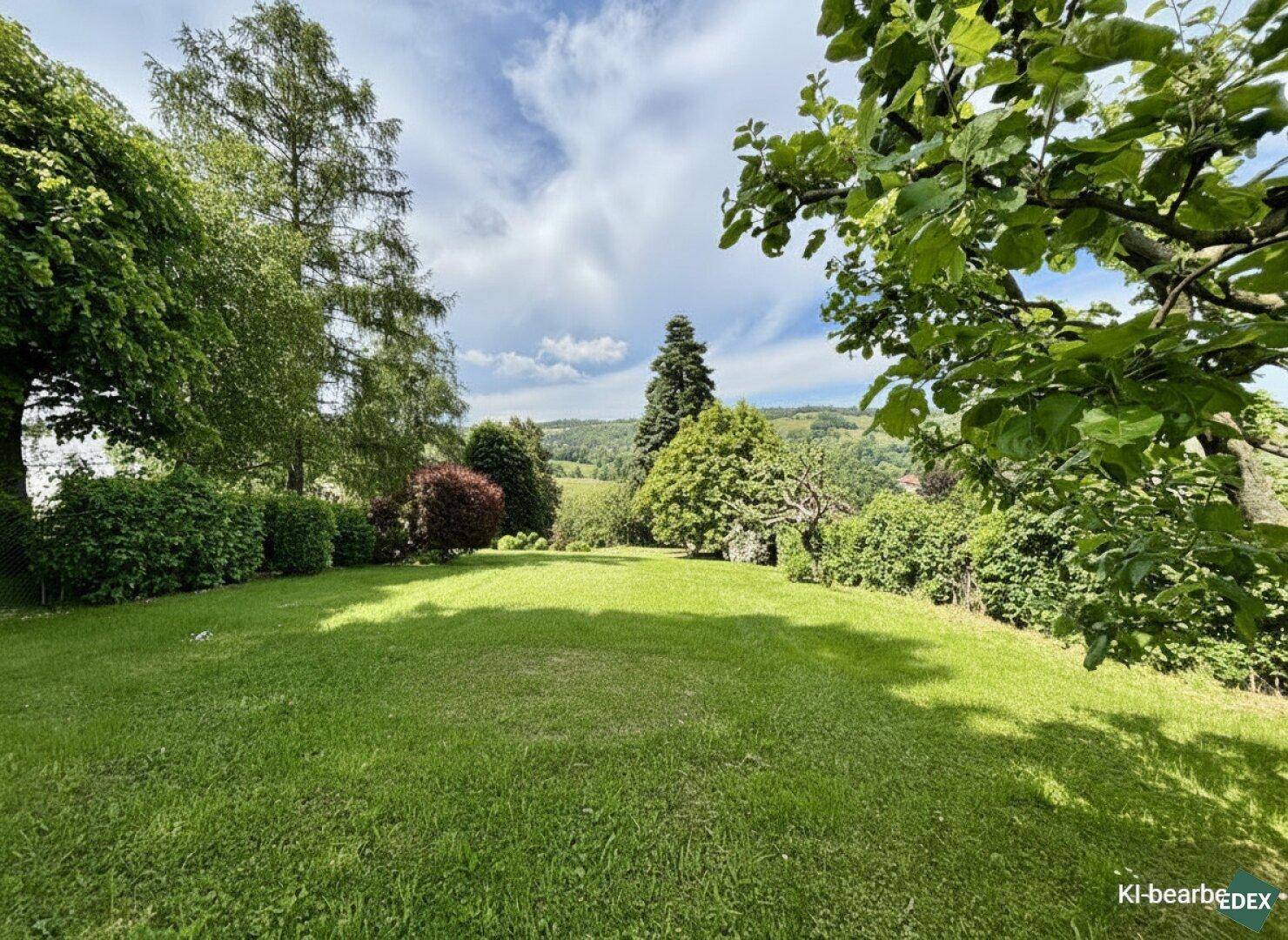 Sonniger Garten mit weitem Rasen und Blick auf die grüne, bewaldete Hügellandschaft.