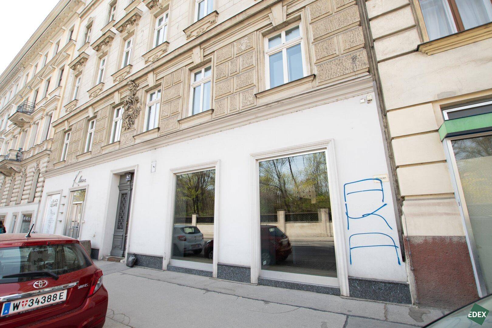 Erdgeschoss eines Gebäudes mit großen Schaufenstern und einer roten Limousine davor an der Straße.