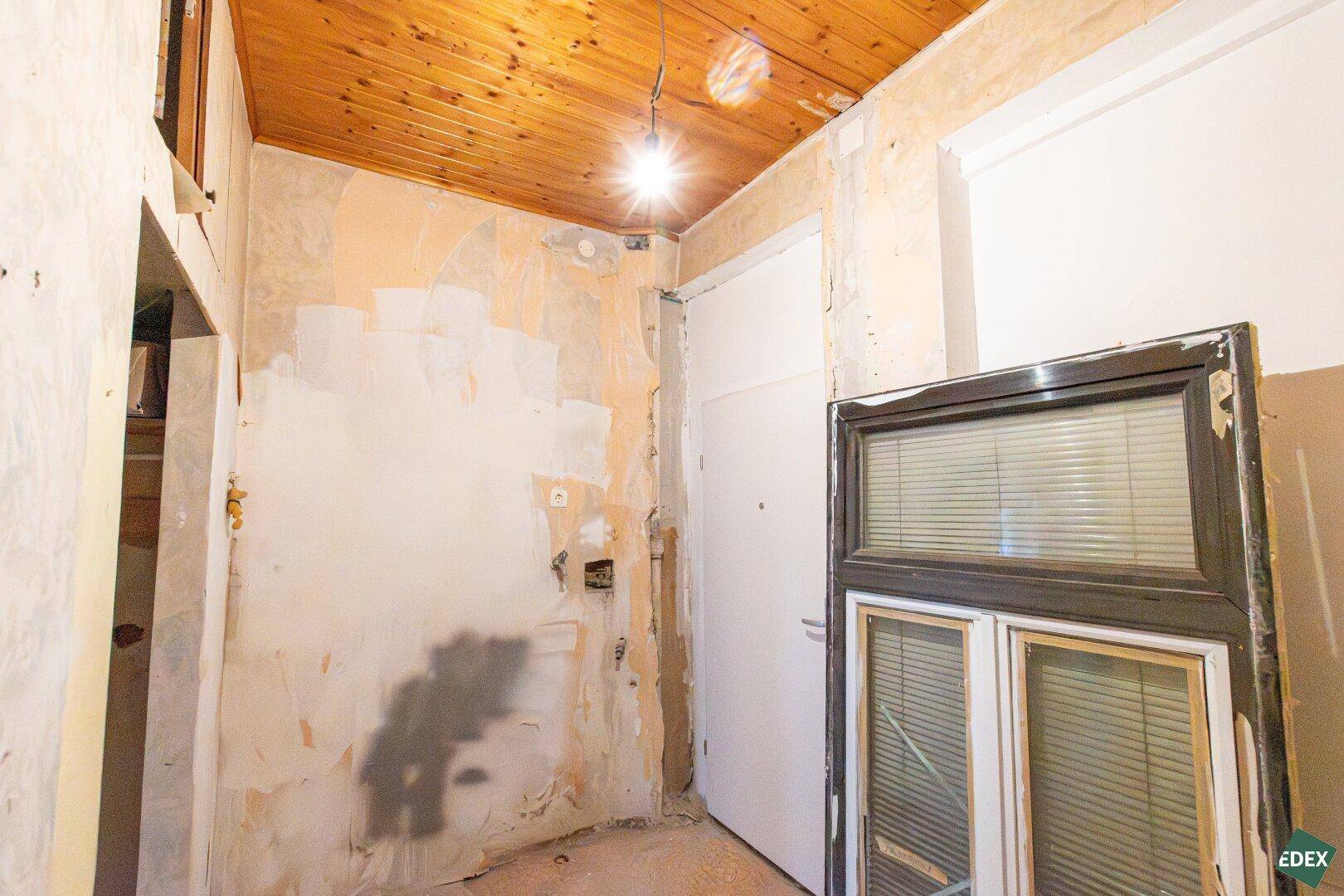 Renovierungsbedürftiger Eingangsbereich mit Holzdecke und abgenutzten Wänden.