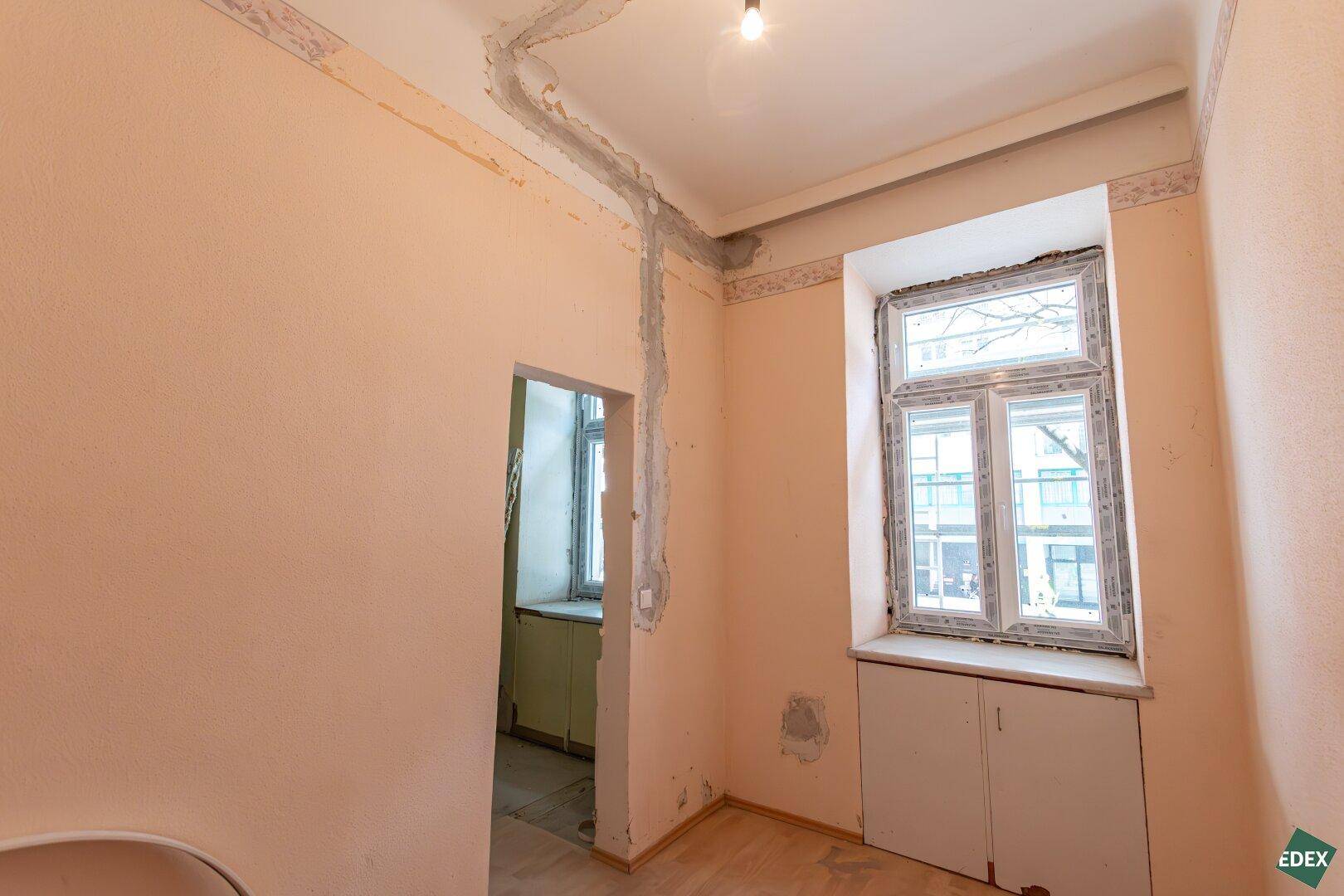 Renovierungsbedürftiger Raum mit rosa Wänden, einem Fenster und sichtbaren Installationsspuren.