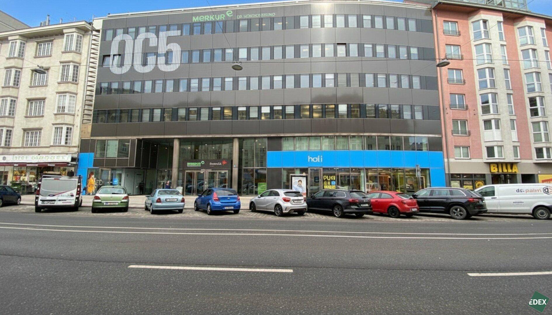 Modernes Bürogebäude mit mehreren Etagen und Geschäften im Erdgeschoss, an einer belebten Straße gelegen.