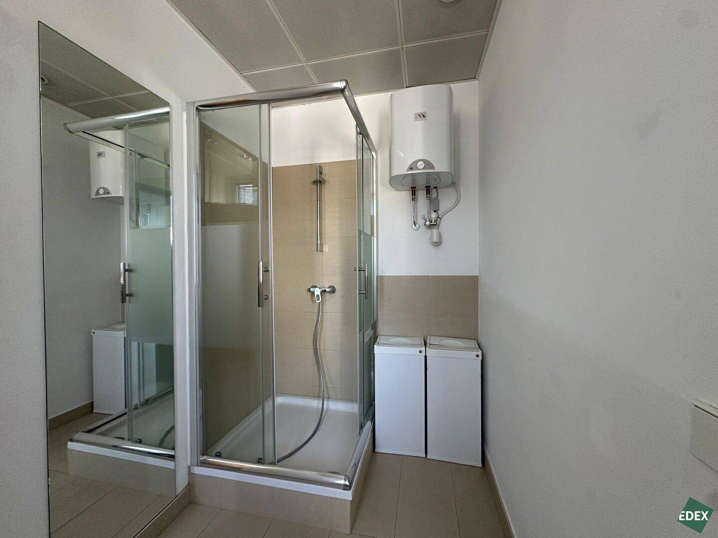 Kleines Badezimmer mit Duschkabine und Warmwasserboiler, funktional und sauber gehalten.
