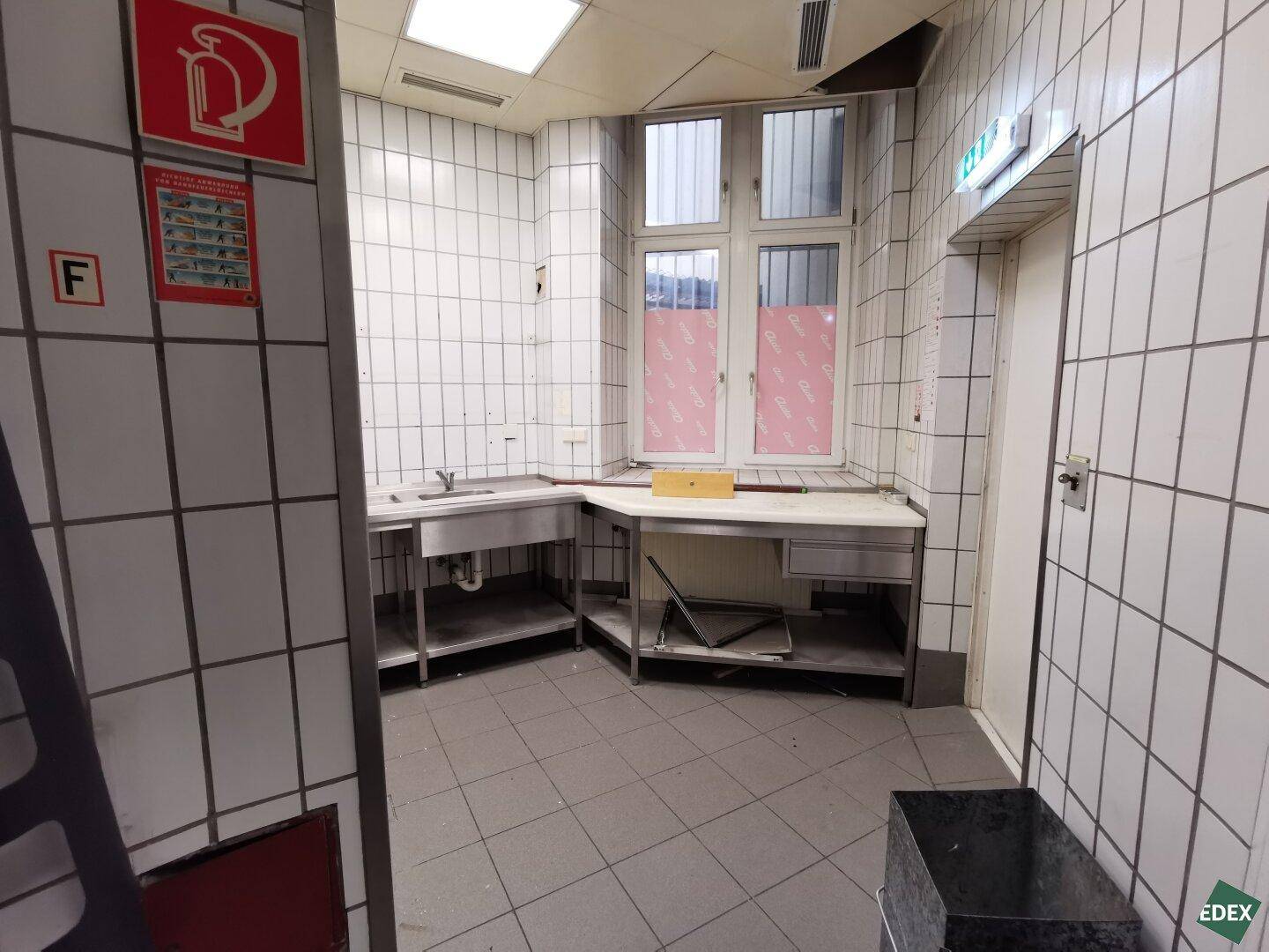 Gewerbliche Küche mit Edelstahlspülen, Arbeitsflächen und einem Fenster mit Gitter.