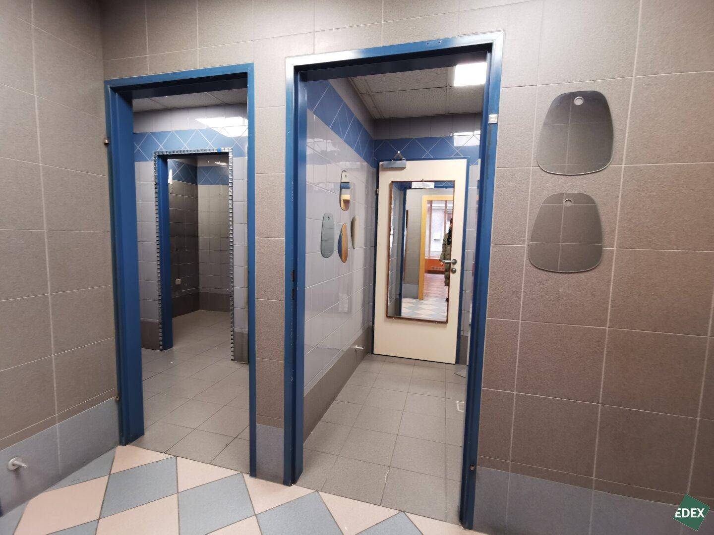 Umkleidebereich oder Flur mit blau-grauen Fliesen und mehreren Türöffnungen.