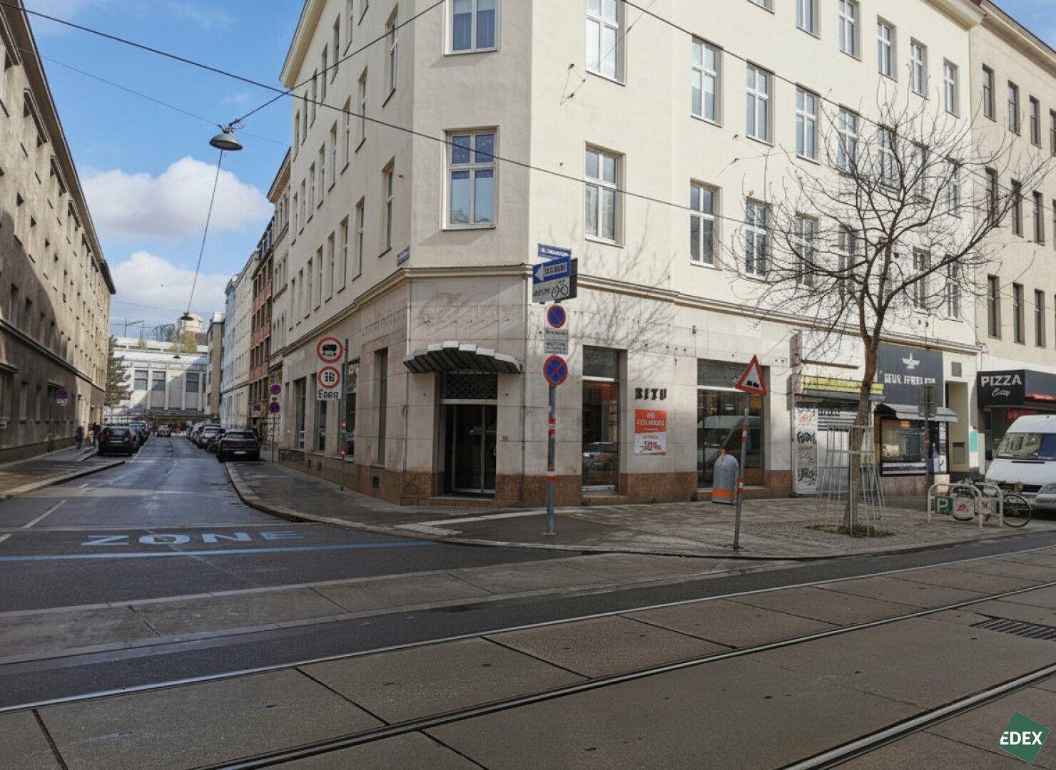 Außenansicht des Eckgebäudes mit Straßenbahnlinien und umliegender Stadtbebauung.