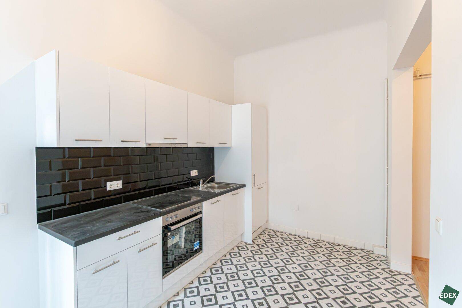 Moderne Einbauküche mit weißen Schränken, schwarzer Arbeitsplatte und gemustertem Fliesenboden.