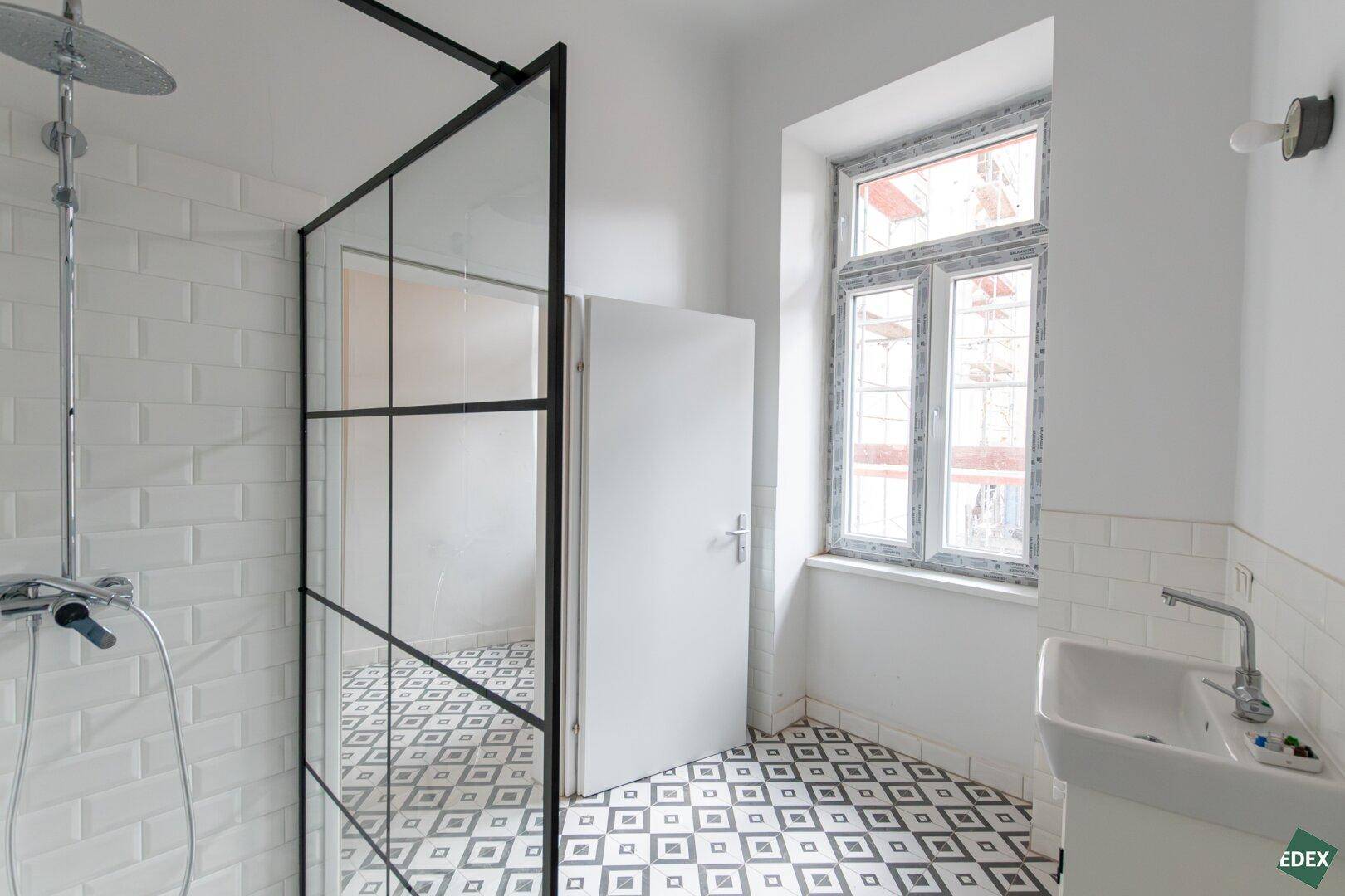 Helles Badezimmer mit begehbarer Dusche, Fenster und modernem Fliesenboden.