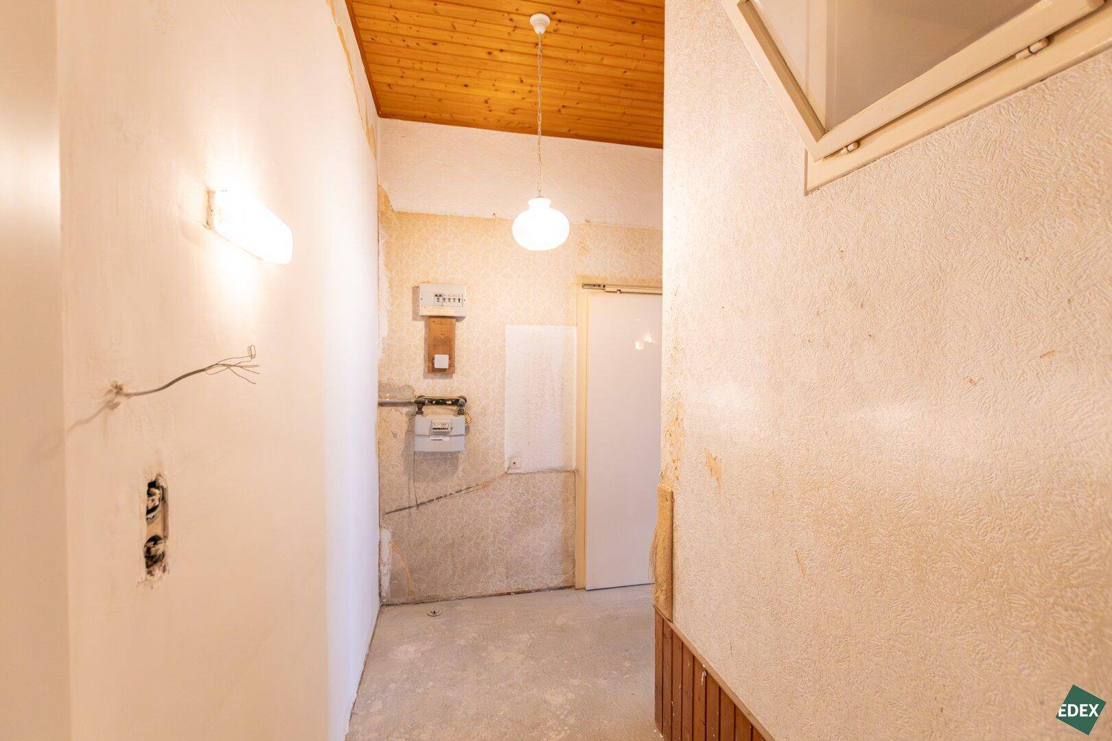 Eingangsbereich mit Holzdecke und einfacher Beleuchtung, der auf eine Renovierung wartet.
