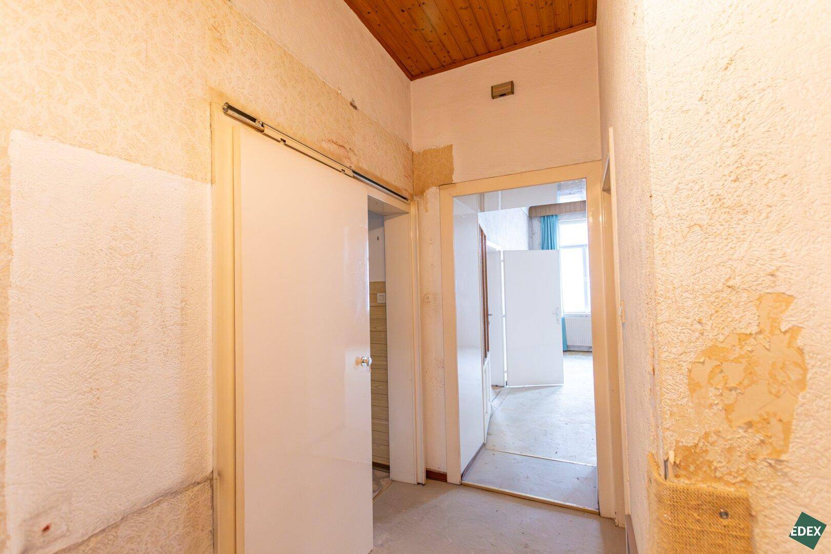 Flur mit Holzdecke und abgenutzter Tapete, der zu weiteren Zimmern führt.
