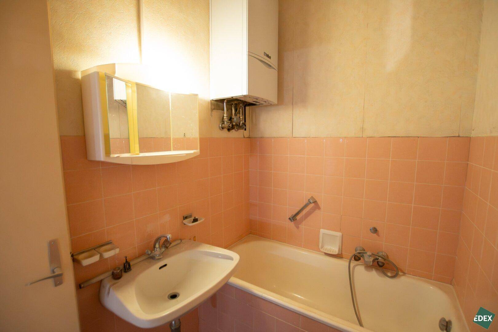 Badezimmer mit rosa Fliesen, Badewanne und Waschbecken, das eine Modernisierung erfordert.