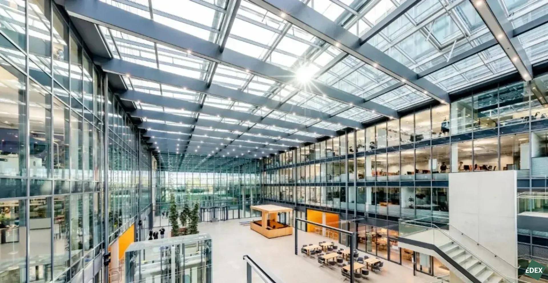 Großzügiges, modernes Atrium mit Glasdach, viel Tageslicht und mehreren Büroetagen in einem Geschäftsgebäude.