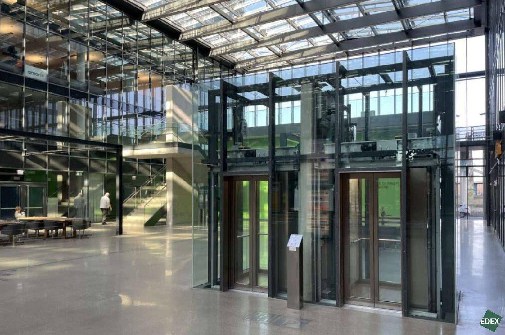 Geräumige, moderne Lobby mit Glasaufzügen, hohen Decken und viel Tageslicht.