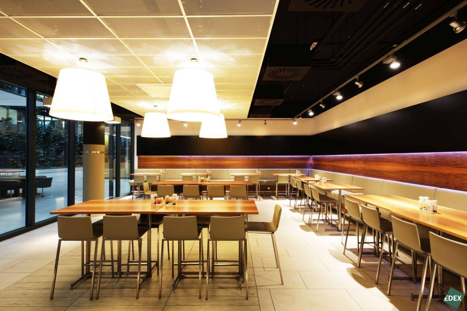 Moderner Restaurantbereich mit Holztischen, bequemen Sitzbänken und stilvollen Hängelampen, ideal für Pausen und Mahlzeiten.