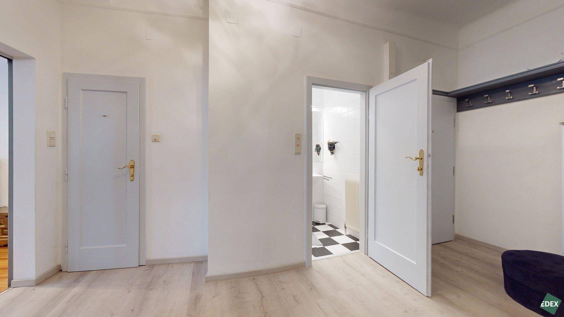Flur mit hellem Boden, Garderobe und offenem Zugang zu einem Badezimmer mit markanten Fliesen.