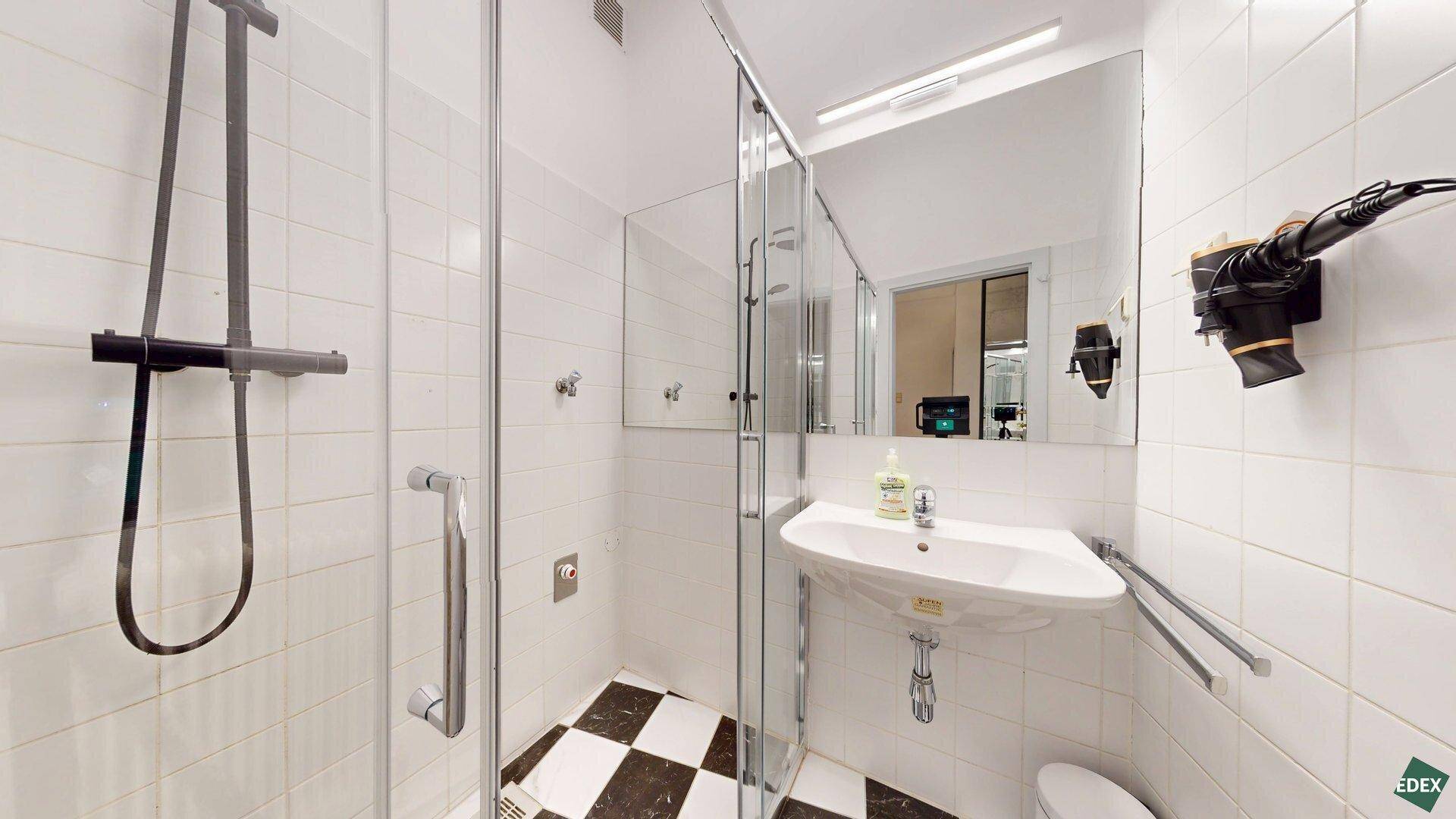 Modernes Badezimmer mit Duschkabine, Waschbecken, großem Spiegel und schwarz-weißem Fliesenboden.