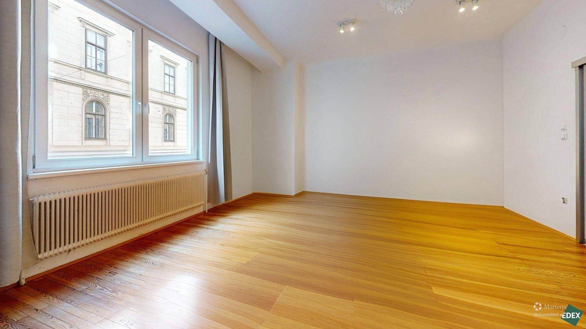 Leerer Raum mit glänzendem Holzboden und einem großen Fenster, das viel Licht hereinlässt.