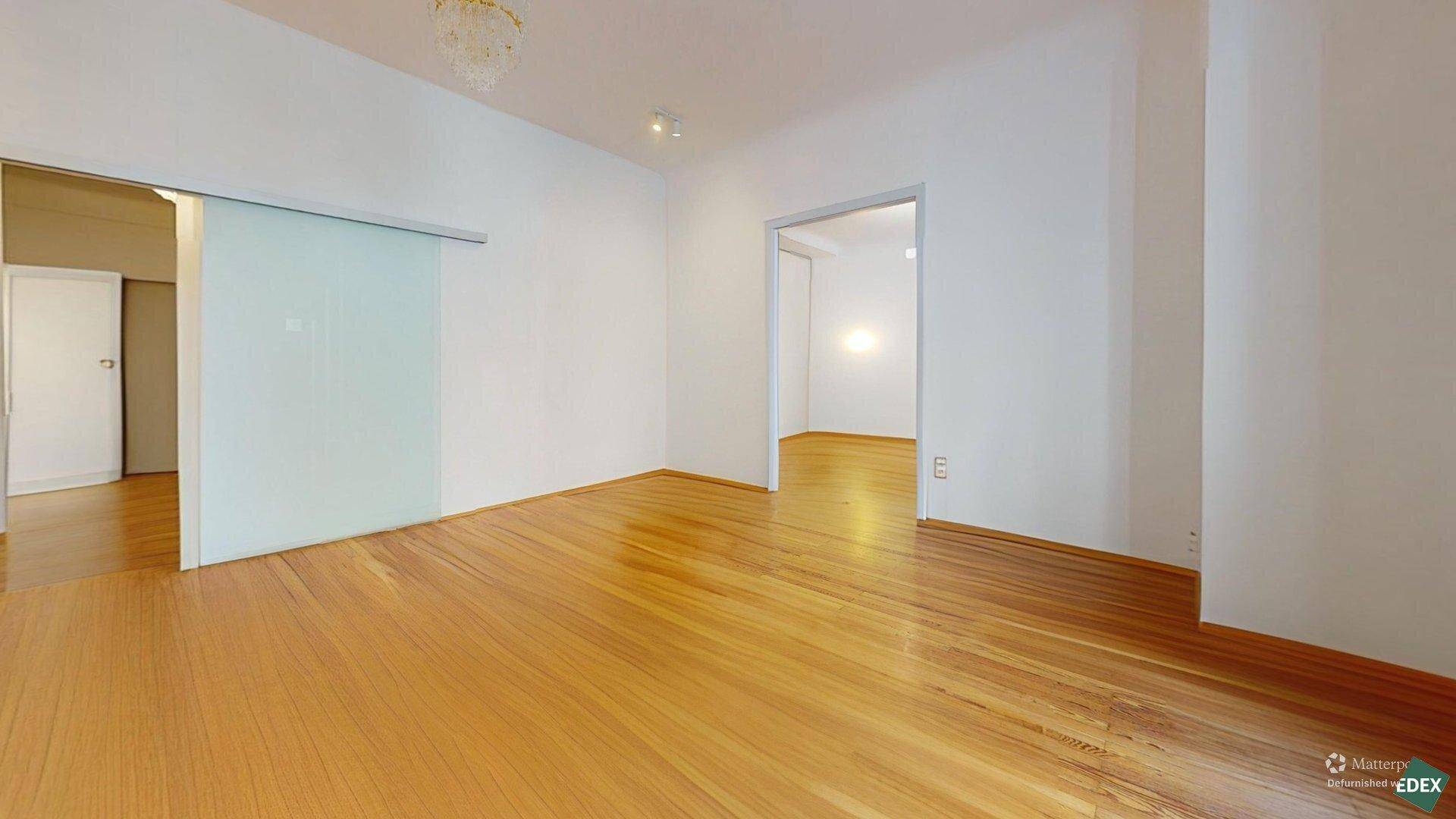 Heller, leerer Raum mit Holzboden, Schiebetür aus Glas und Zugang zu einem weiteren Zimmer.