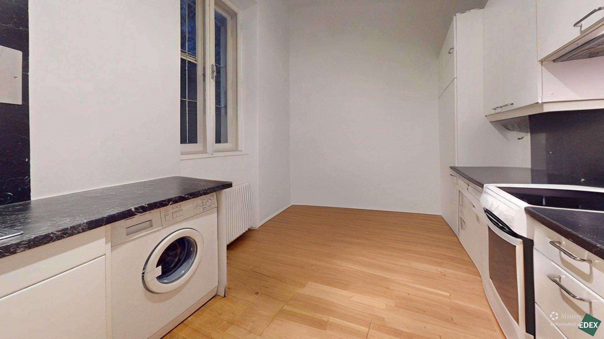 Geräumige Küche mit weißen Schränken, Herd, Waschmaschine und einem Fenster für Tageslicht.