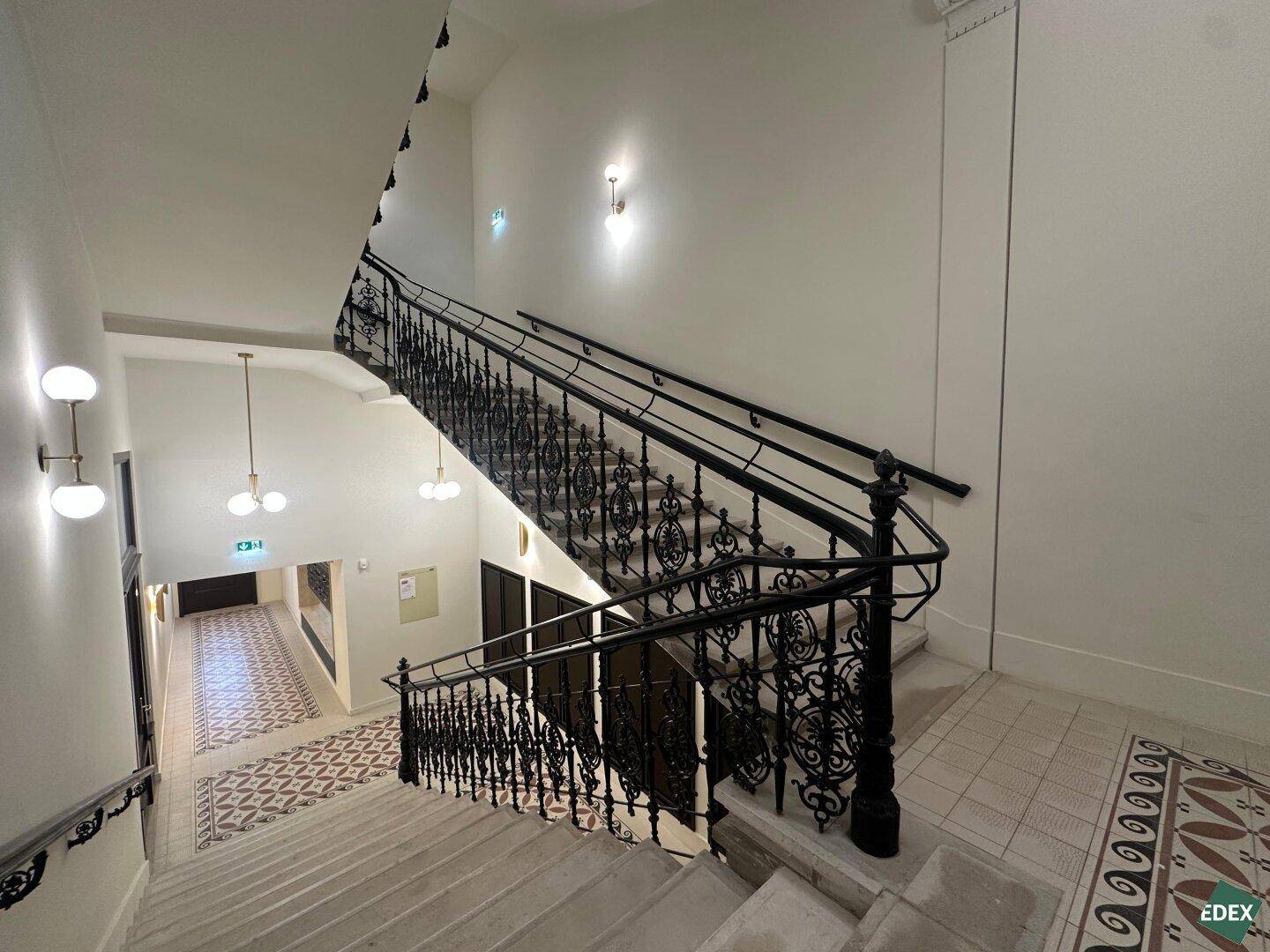 Historisches Treppenhaus mit kunstvollem schmiedeeisernem Geländer und gemusterten Fliesen.