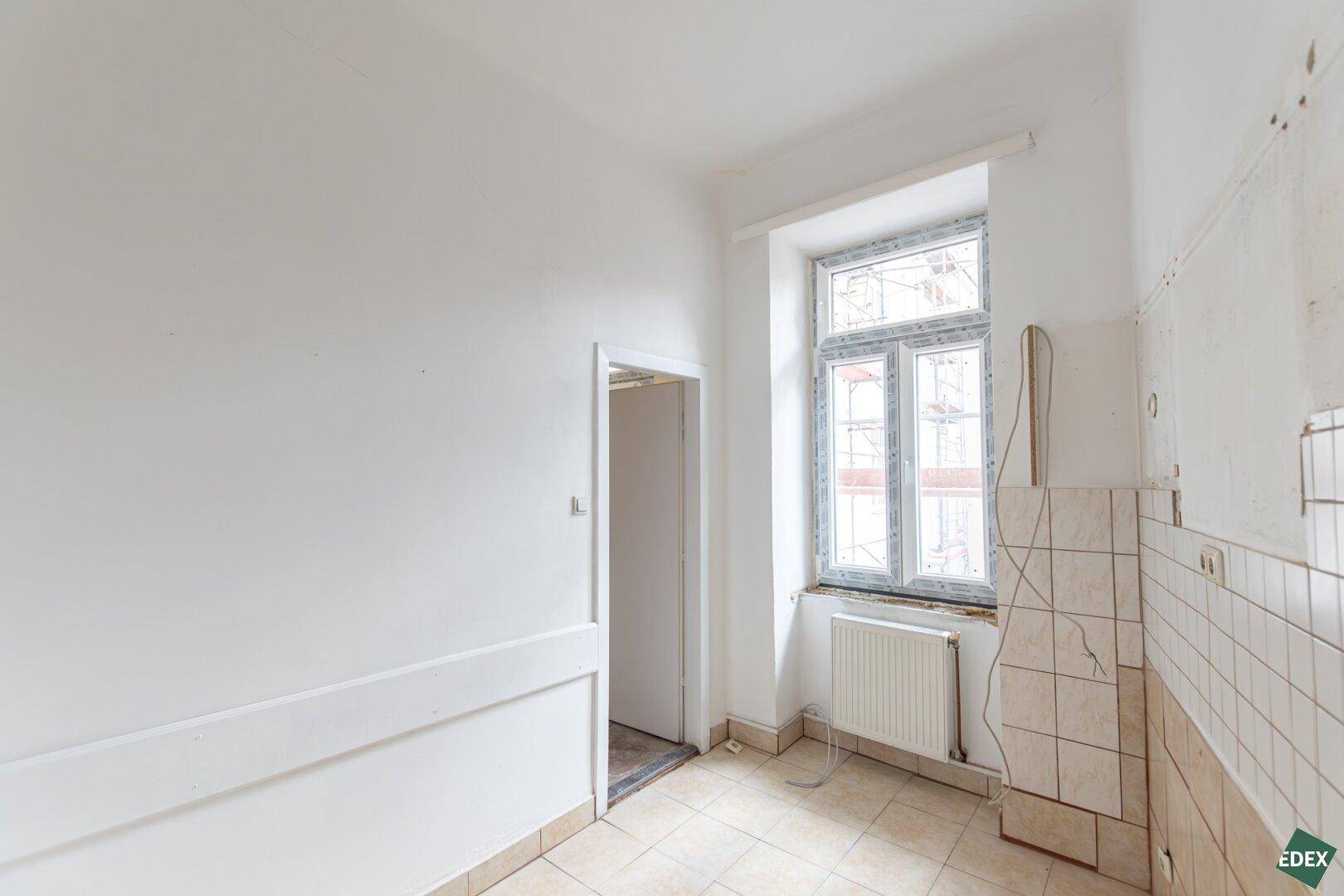 Heller Raum mit weißen Wänden, Fliesenboden und einem Fenster, bereit für eine Kücheninstallation.