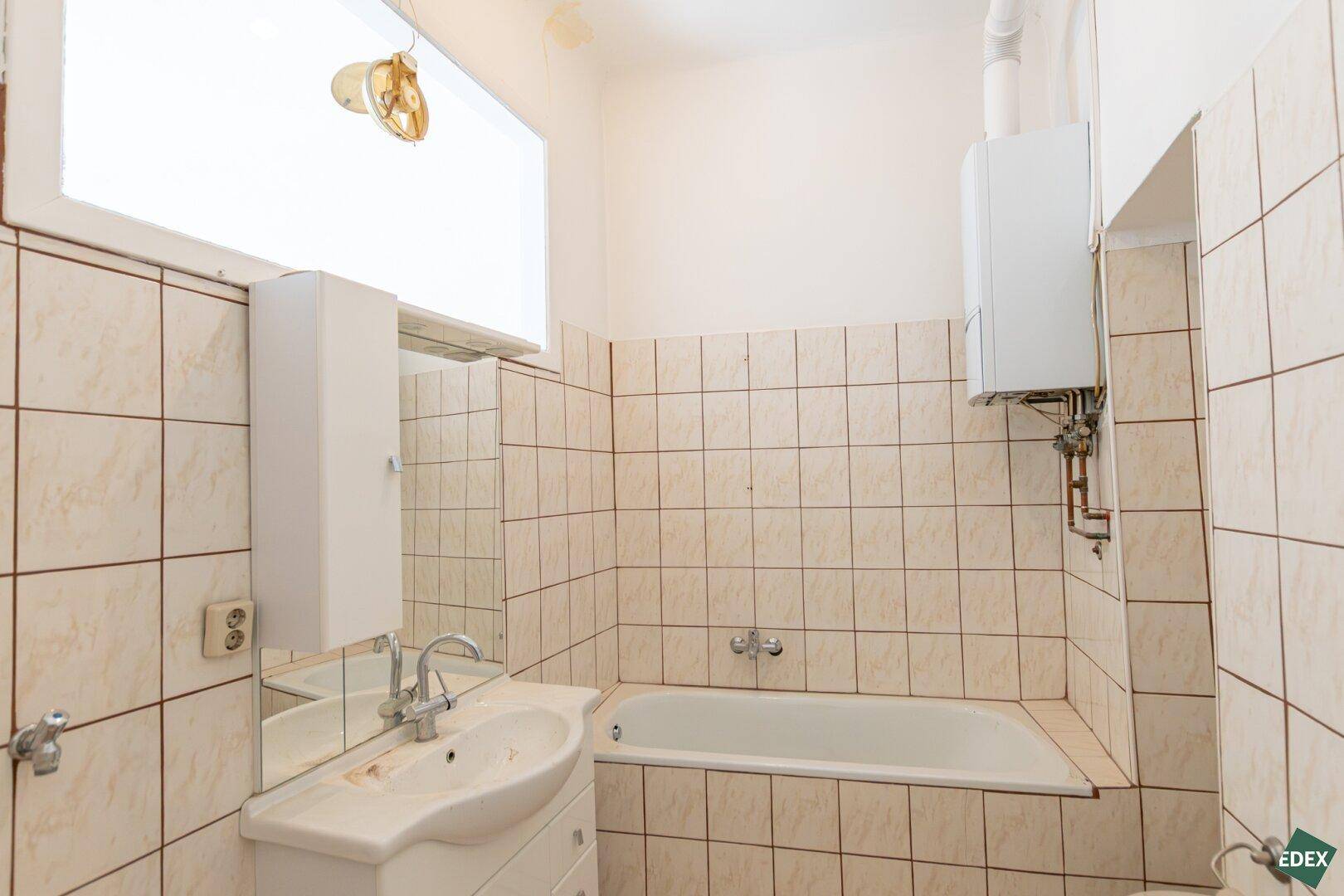 Badezimmer mit beigefarbenen Fliesen, Badewanne, Waschbecken und Gastherme.